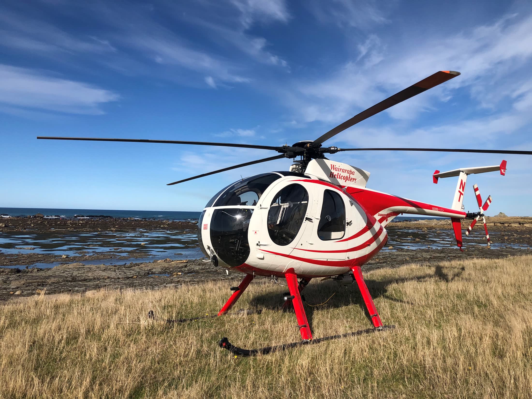A red and white Wairarapa helicopter beside the wild Wairarapa coast
